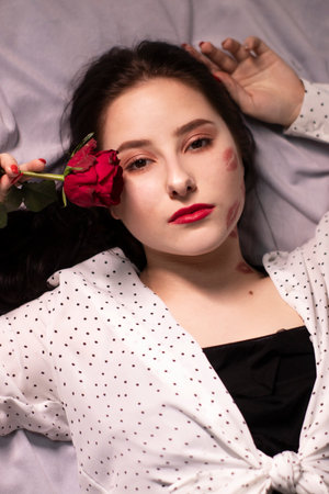 sexy brunette woman with kisses, lipstick marks on her face and neck, with red rose. girlfriend, date, relashionship. lesbian gay. lgbt. copy spaceの写真素材