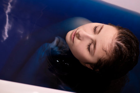 portrait of attractive brunette woman topless in blue liquid. in bathtub with colored water....