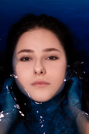 portrait of attractive brunette woman topless in blue liquid. in bathtub with colored water....