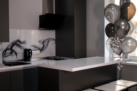 Corner of stylish Minimalistic grey kitchen, dark gray cupboards, white countertops and bar with stools. black sink, kettle and stove. and black and white balloons. High quality photoの写真素材