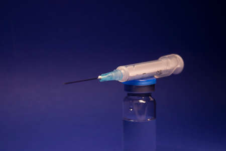 Vaccine bottle phial with no label, medical syringe injection needle. isolated on blue background....