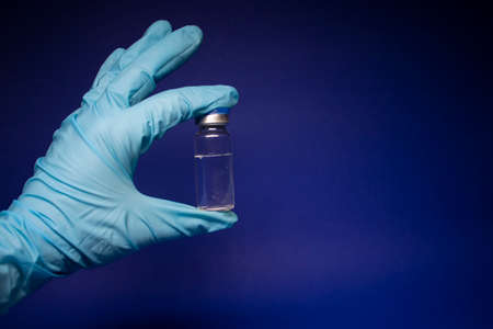 Development of vaccine. bottle phial with no label in blue medical glove. isolated on blue background. cure. copy space. Vaccination for prevention and treatment to infectionsの写真素材