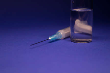 Vaccine bottle phial with no label, medical syringe injection needle. isolated on blue background. Development of vaccine . cure. World race in researching. copy spaceの写真素材