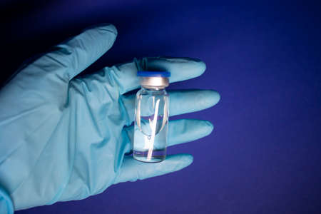 Development of vaccine . bottle phial with no label in blue medical glove. isolated on blue...