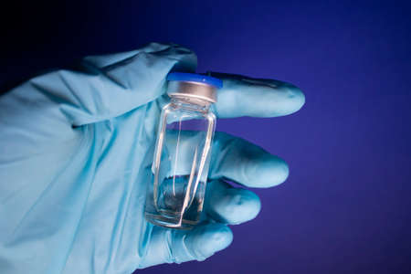Development of vaccine . bottle phial with no label in blue medical glove. isolated on blue background. cure. copy space. Vaccination for prevention and treatment to infectionsの写真素材