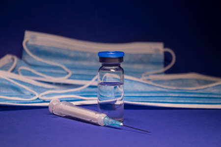 Vaccine bottle phial with no label and medical syringe with injection needle on background of blue...