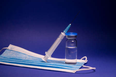 Vaccine bottle phial with no label on blue medical mask and medical syringe with injection needle....