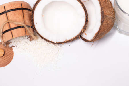 opened coconut near coconut flakes in wooden bowl and glass of coconut milk isolated on white...