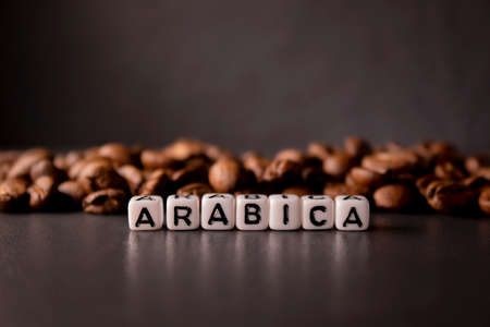 close up of Freshly roasted coffee beans near word ARABICA written with little white cubes. view...
