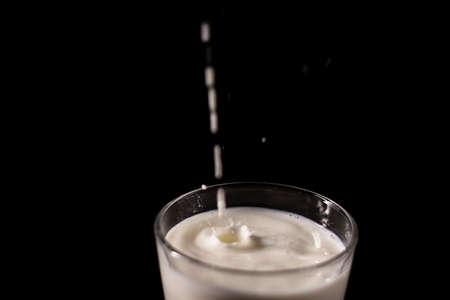 pouring milk in a glass. splash of white liquid isolated on dark background.の写真素材