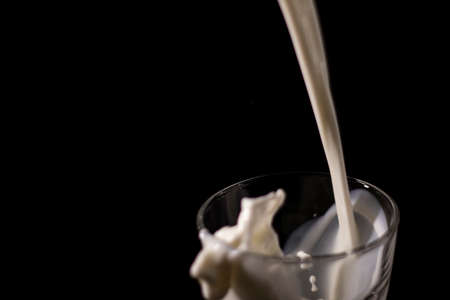 pouring milk in a glass. splash of white liquid isolated on dark background.の写真素材