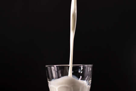 pouring milk in a glass. splash of white liquid isolated on dark background.の写真素材