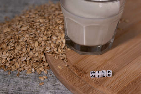 pile of raw oatmeal near a glass of milk near word milk written with little white cubes. healthy breakfast. vegan oat milk.の写真素材