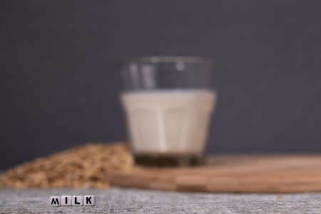 pile of raw oatmeal near a glass of milk near word milk written with little white cubes. healthy breakfast. vegan oat milk.の写真素材