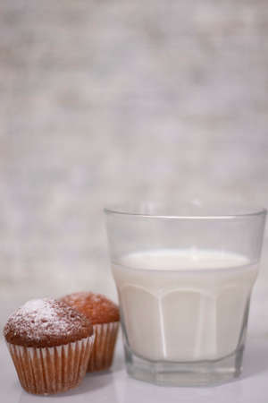 two little cupcakes or muffins in powdered sugar near a glass of milk. healthy breakfast. snack or lunch.の写真素材
