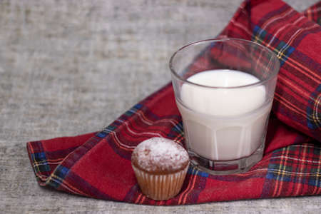 cupcake or muffin in powdered sugar near a glass of milk on plaid red fabric tablecloth. healthy breakfast. snack or lunch.の写真素材
