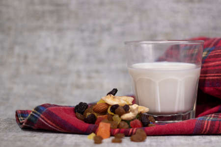 glass of milk near dried fruits, candied fruits, raisins, nuts on plaid red fabric tablecloth. healthy breakfast snack.の写真素材