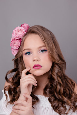 portrait of pretty brunette girl with pink roses in her hair on gray background. flowers in curls on the head. fashion photo. spring, flowering, colors.の写真素材