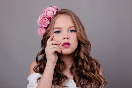 portrait of pretty brunette girl with pink roses in her hair on gray background. flowers in curls on the head. fashion photo. spring, flowering, colors.の写真素材
