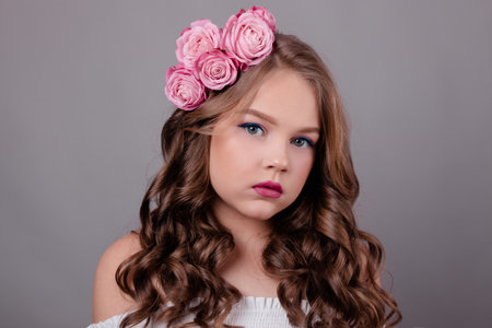 portrait of pretty brunette girl with pink roses in her hair on gray background. flowers in curls on the head. fashion photo. spring, flowering, colors.の写真素材