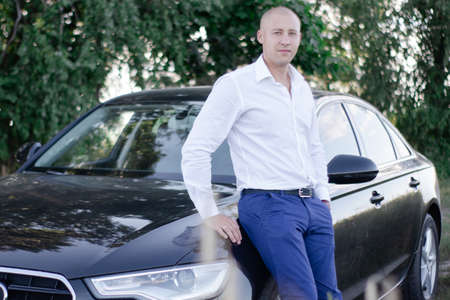 handsome bald man in a suit near luxury car. businessman in automobileの写真素材