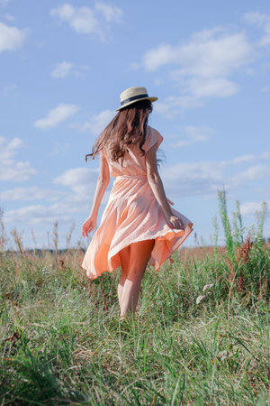 pretty brunette woman in cream dress and a straw hat in the fieldの写真素材