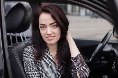 portrait of attractive fabulous brunette woman wearing checkered dress in a lux car. lady in...