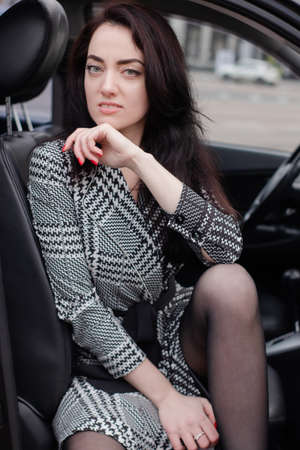 portrait of an attractive brunette in gray checkered dress in a black car. girl in automobile....