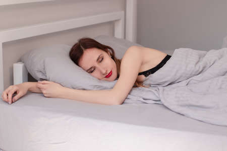 Sexy redhead model in black lingerie is lying on bed with gray sheets.の写真素材