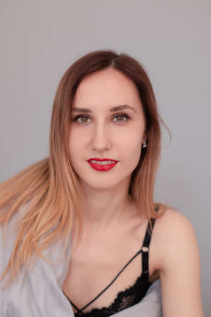 portrait of pretty redhead woman in black lingerie on bed with gray sheets and blanket.の写真素材