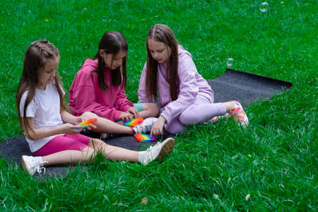 three teenage girls play with trendy sensory toy pop it outdoors on grass. Push pop bubble flexible fidget sensory toy. Stress and anxiety relief. Trendy silicon game for stressed children and adults.の写真素材