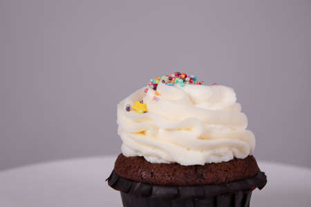 tasty chocolate cupcake with white topping cream on a white stand on a gray background. sweets,...