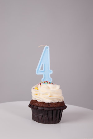 tasty chocolate cupcake with white topping cream and candle in shape of number four 4.on a white...