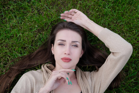 charming brunette lies on green grass. Tired, serious.