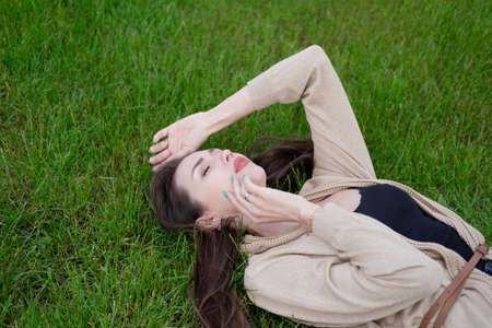 charming brunette lies on green grass. Tired, serious.