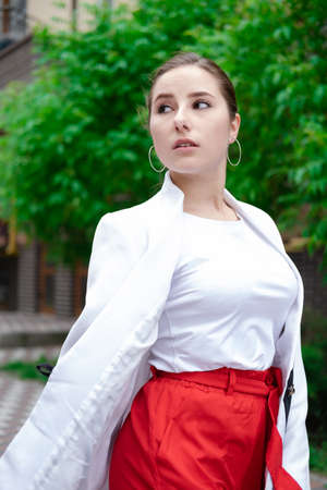 confident brunette woman in red pants and white blouse and jacket walking in the street.の写真素材