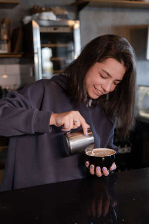 cute girl makes latte in coffee shop. Barista making coffee. Draws a drawing with milk on drink - cappuccino.の写真素材