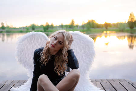 woman with white angel wings. wearing black leather clothes. fallen dark angel. demon. beast. girl in angel costumeの写真素材