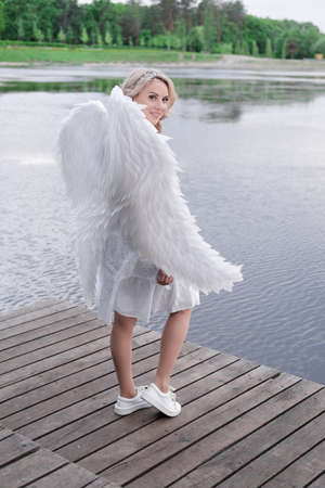 beautiful angel in white dress. Amazing blond woman with long curly hair and white wingsの写真素材