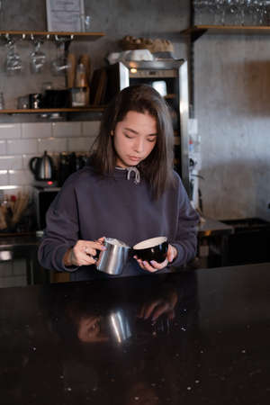 cute girl makes latte in coffee shop. Barista making coffee. Draws a drawing with milk on drink - cappuccino.の写真素材
