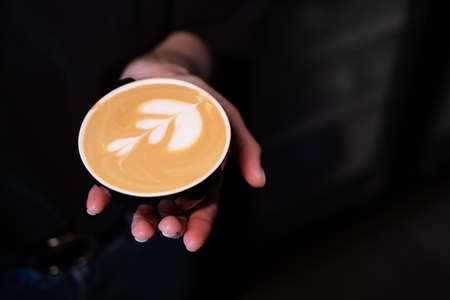 hand holding Hot coffee cup with flower shape latte coffee art. coffee house concept. Coffee for you...