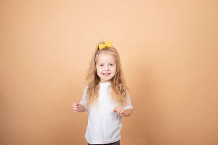portrait of a sweet blonde little girl in white t-shirt and with yellow bow on her head. on brown background.の写真素材