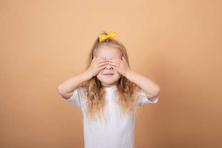 portrait of a sweet blonde little girl in white t-shirt and with yellow bow on her head. on brown background.の写真素材
