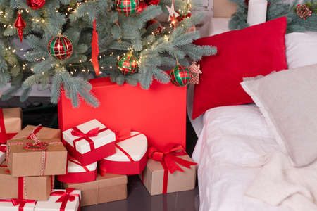 stylish christmas room. red and white colors. christmas tree with balls and bubbles and tinsel on it. pile of presents near with pretty bows. white brick wall. trendy colors. happy new year.の写真素材
