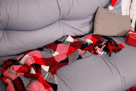 cozy christmas photo zone. gray sofa with red checkered blanket. red garland on white brick wall. red gift box and toy santa claus.の写真素材