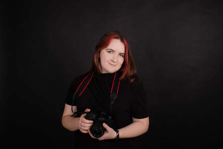 redhead girl with a professional camera posing on black background. woman female photographer
