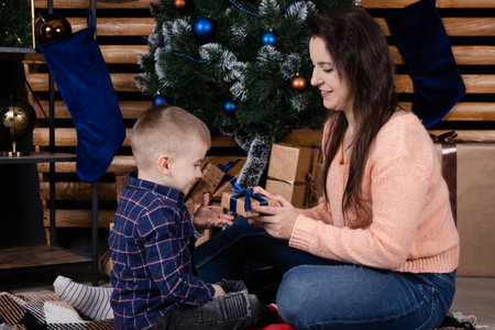 Young mother in a beige knitted sweater near a Christmas tree with her son. single mother with child. family time. mothers love.の写真素材
