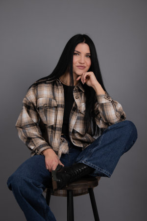 portrait of beautiful young woman in brown checkered shirt and jeans on gray background. pretty...