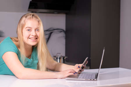 Young businesswoman in green using smartphone. On desk is laptop. Girl working, learning online. Social media, network. Online marketing, educationの写真素材