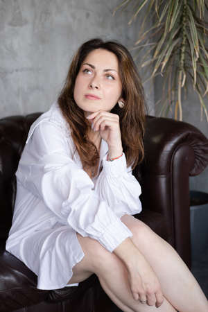 confident brunette woman in white shirt on leather couch.